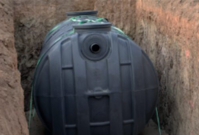 Depósito de polietileno negro colocado en una zanja durante la instalación de un reactor biológico