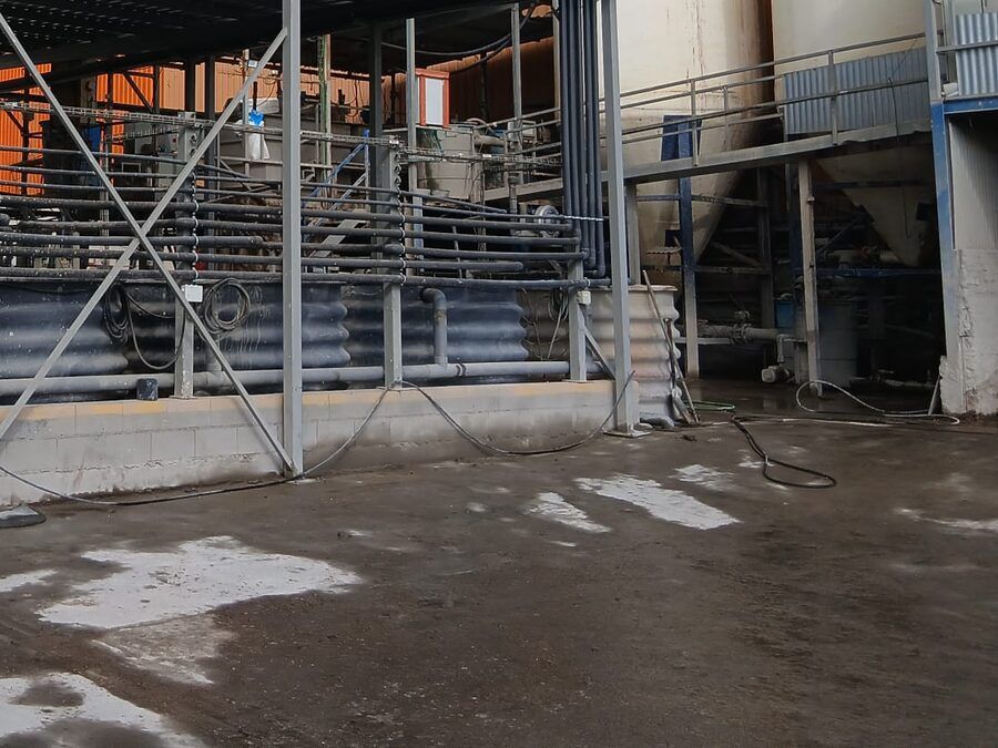 Instalación industrial con depósitos corrugados, tuberías y estructura metálica bajo una cubierta